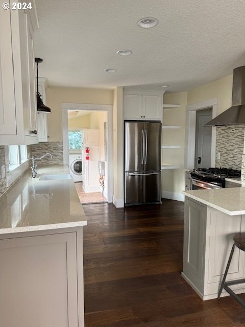 kitchen with dark hardwood / wood-style floors, decorative backsplash, appliances with stainless steel finishes, washer / dryer, and wall chimney exhaust hood