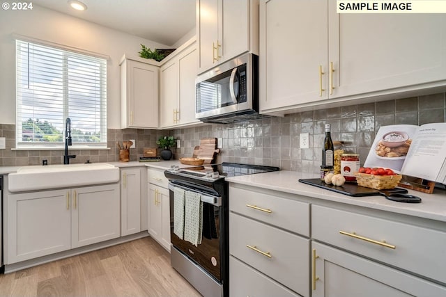 kitchen with sink, light hardwood / wood-style flooring, backsplash, white cabinets, and appliances with stainless steel finishes