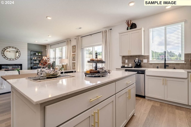 kitchen with a large fireplace, sink, light hardwood / wood-style flooring, dishwasher, and a kitchen island