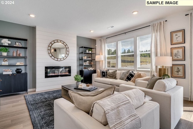 living room with a textured ceiling, a large fireplace, and light hardwood / wood-style flooring