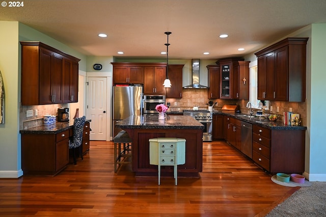 kitchen featuring appliances with stainless steel finishes, a center island, dark hardwood / wood-style flooring, and wall chimney exhaust hood