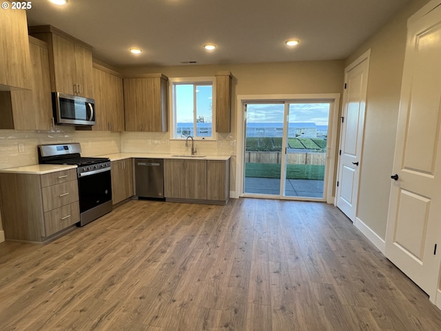 kitchen with stainless steel appliances, sink, light hardwood / wood-style flooring, and backsplash