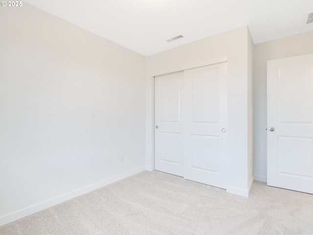 unfurnished bedroom featuring light carpet, baseboards, visible vents, and a closet