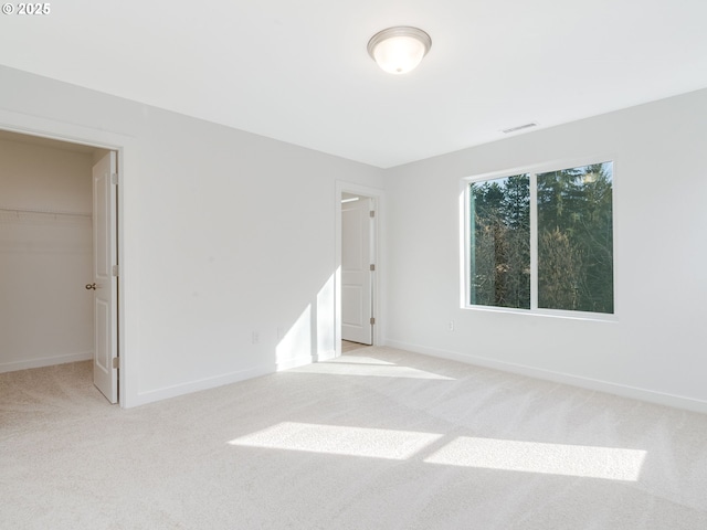 unfurnished bedroom with carpet, visible vents, a walk in closet, and baseboards