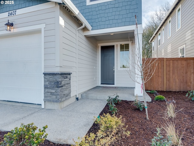 entrance to property featuring an attached garage and fence