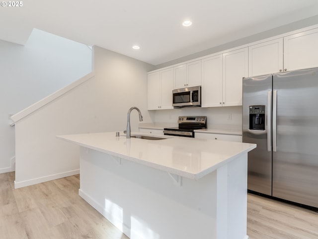 kitchen with light countertops, appliances with stainless steel finishes, white cabinets, a sink, and light wood-type flooring