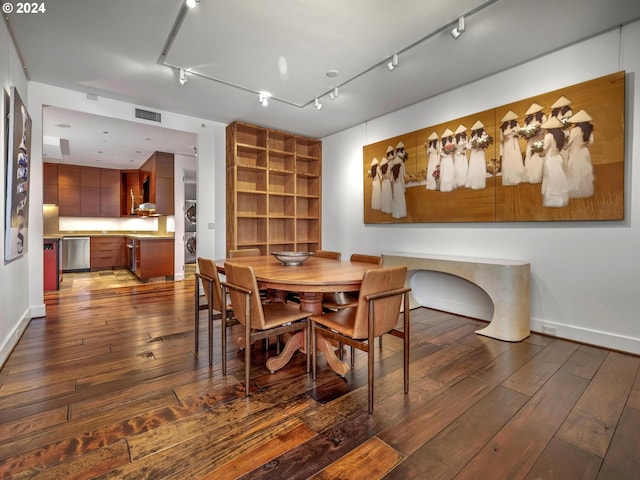 dining area with dark wood-type flooring, rail lighting, and stacked washer and clothes dryer