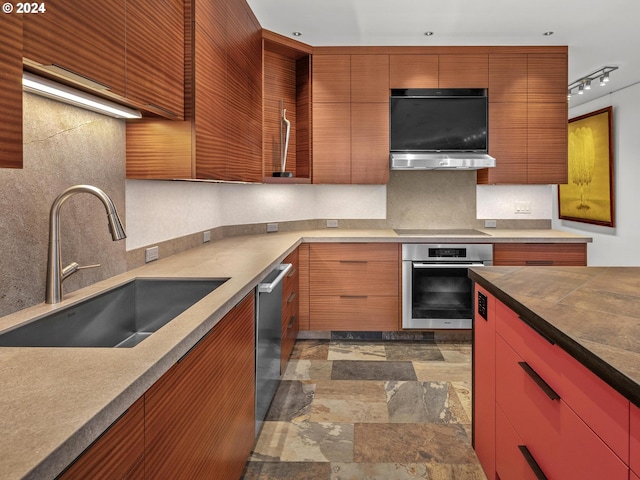 kitchen featuring range hood, appliances with stainless steel finishes, tasteful backsplash, sink, and track lighting