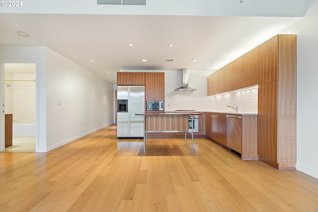 kitchen with stainless steel appliances, tasteful backsplash, light wood-style floors, wall chimney range hood, and modern cabinets