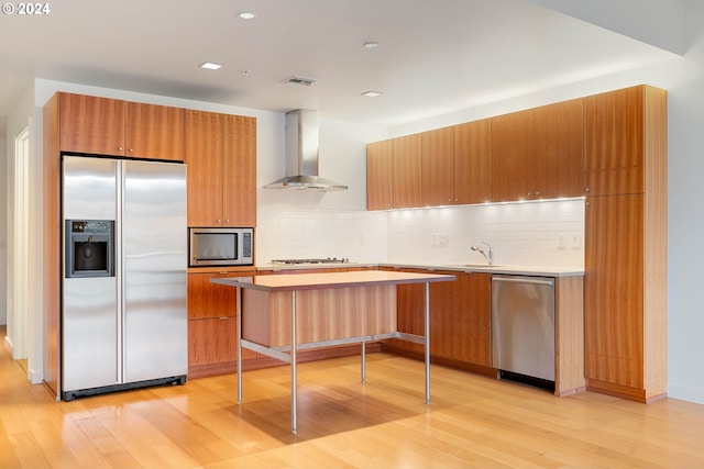 kitchen featuring decorative backsplash, wall chimney exhaust hood, a kitchen breakfast bar, stainless steel appliances, and light hardwood / wood-style floors