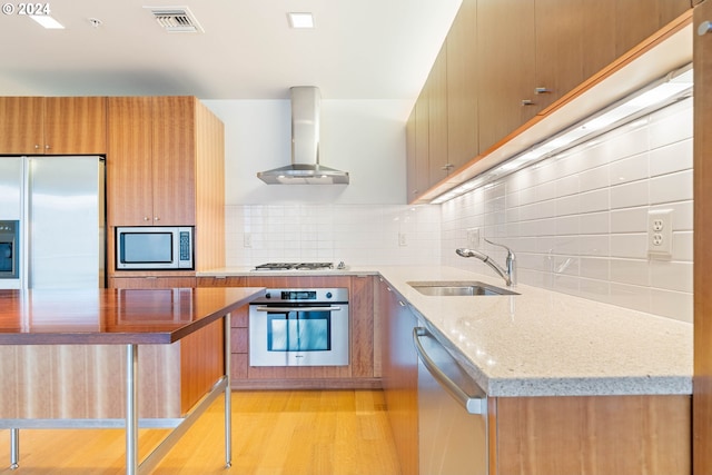 kitchen featuring light stone counters, a sink, visible vents, appliances with stainless steel finishes, and wall chimney exhaust hood