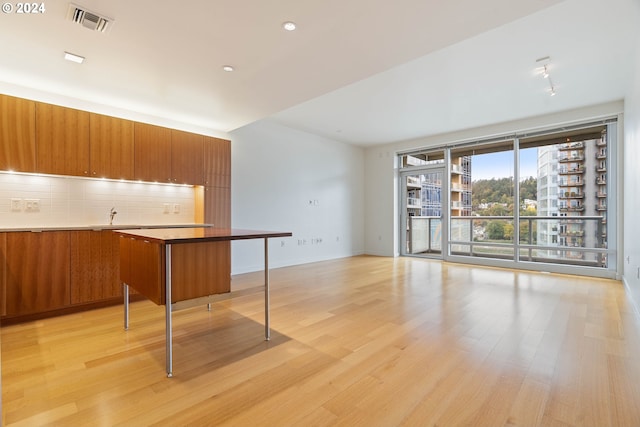 kitchen featuring brown cabinets, light wood finished floors, visible vents, decorative backsplash, and modern cabinets