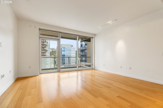 spare room featuring light wood-type flooring, rail lighting, baseboards, and a city view