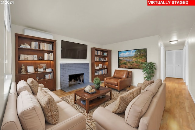 living room featuring a fireplace, light hardwood / wood-style flooring, and a wall mounted AC