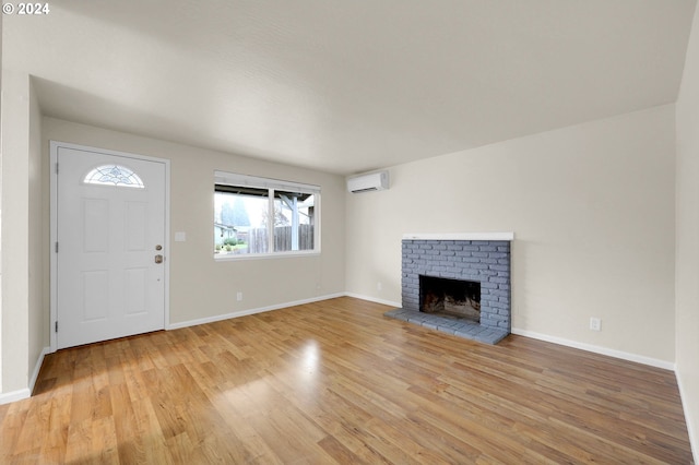 unfurnished living room with a fireplace, a wall mounted AC, and light hardwood / wood-style flooring