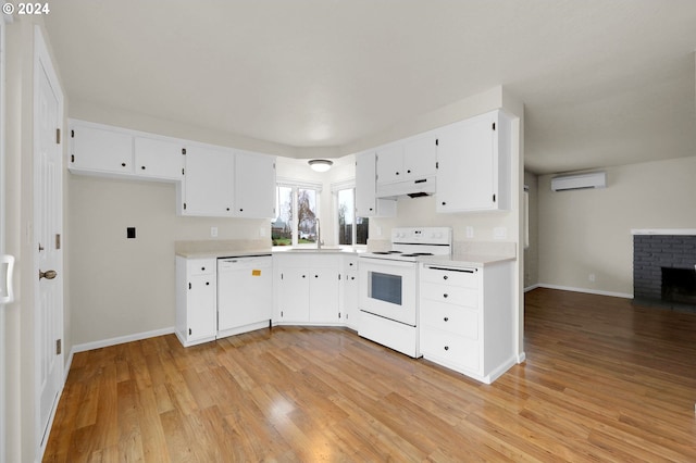 kitchen with a wall mounted AC, white cabinets, light hardwood / wood-style floors, and white appliances