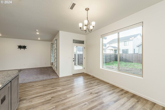 unfurnished dining area featuring a textured ceiling, an inviting chandelier, and light hardwood / wood-style flooring