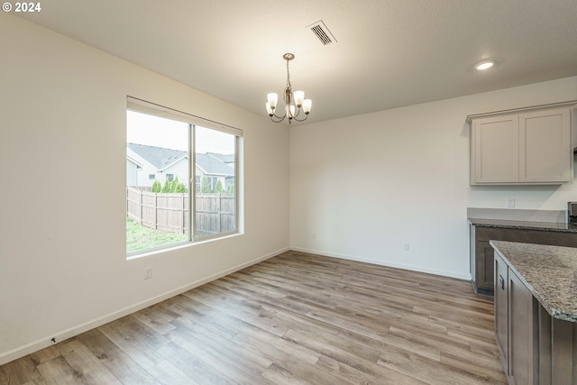 unfurnished dining area with light hardwood / wood-style floors, a textured ceiling, and a chandelier