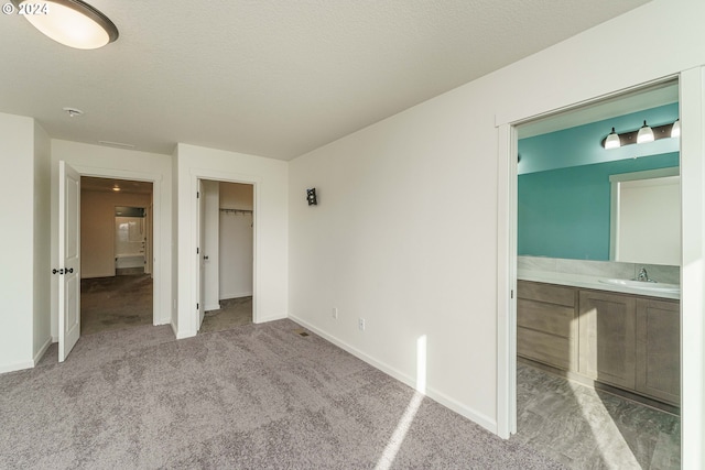 unfurnished bedroom with ensuite bath, a closet, sink, and light colored carpet