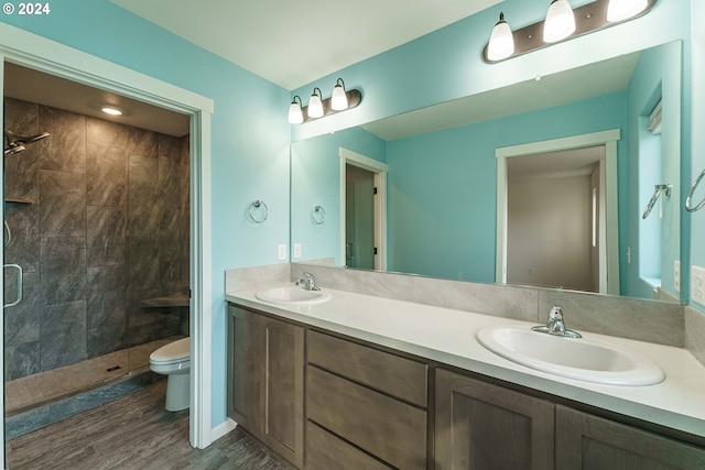 bathroom with a tile shower, vanity, wood-type flooring, and toilet