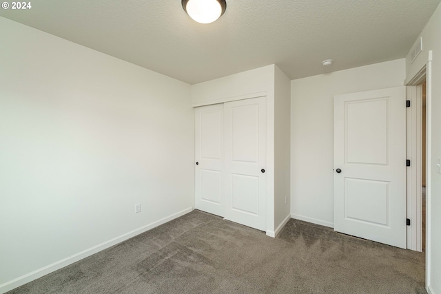 unfurnished bedroom with dark carpet, a textured ceiling, and a closet