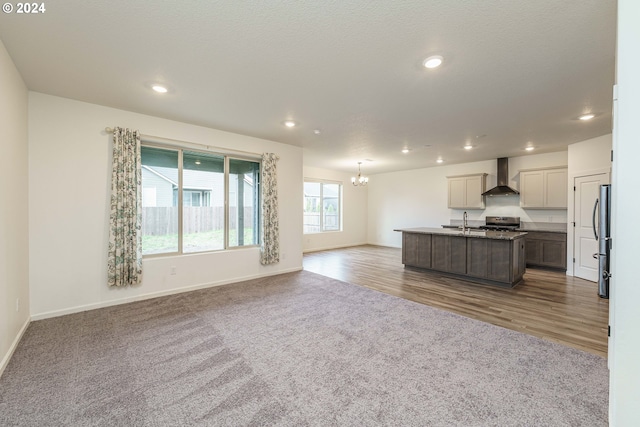 kitchen with a center island with sink, sink, hardwood / wood-style flooring, wall chimney exhaust hood, and appliances with stainless steel finishes