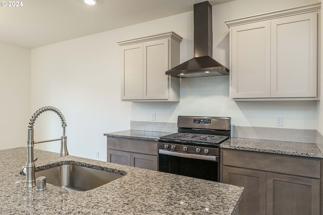 kitchen with gas stove, light stone counters, sink, and wall chimney range hood