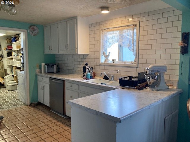 kitchen featuring tasteful backsplash, white cabinetry, stainless steel dishwasher, and sink