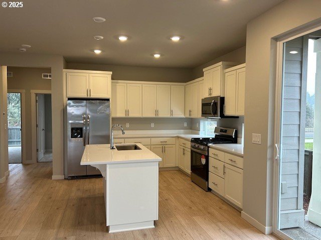 kitchen featuring stainless steel appliances, an island with sink, a sink, and light wood-style flooring