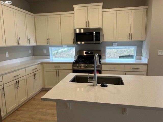 kitchen with appliances with stainless steel finishes, white cabinetry, light wood-type flooring, and sink