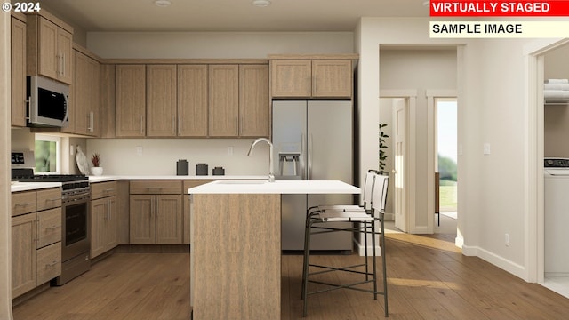 kitchen featuring stainless steel appliances, sink, light wood-type flooring, an island with sink, and a breakfast bar