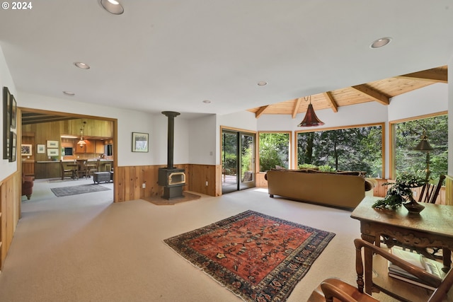 carpeted living room with lofted ceiling with beams, a wood stove, and wooden walls