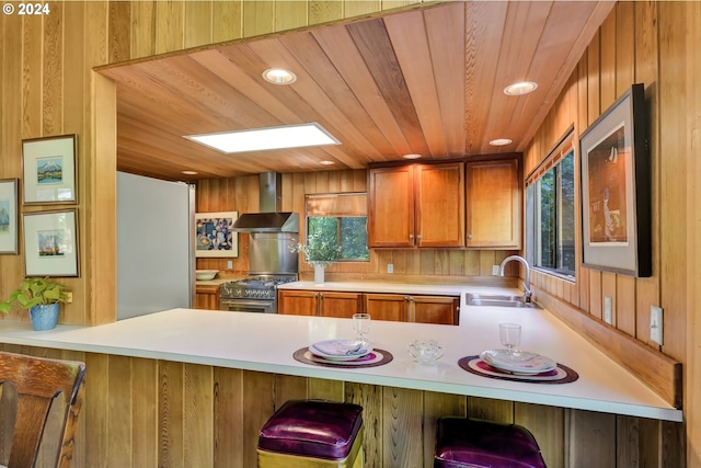 kitchen with sink, wall chimney exhaust hood, high end stove, kitchen peninsula, and wood ceiling