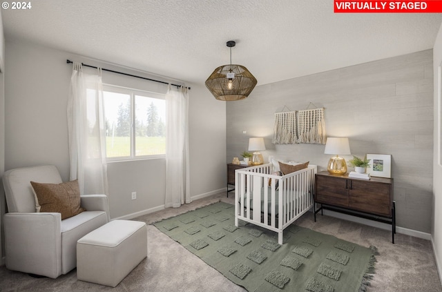 bedroom featuring a textured ceiling, a crib, and carpet flooring