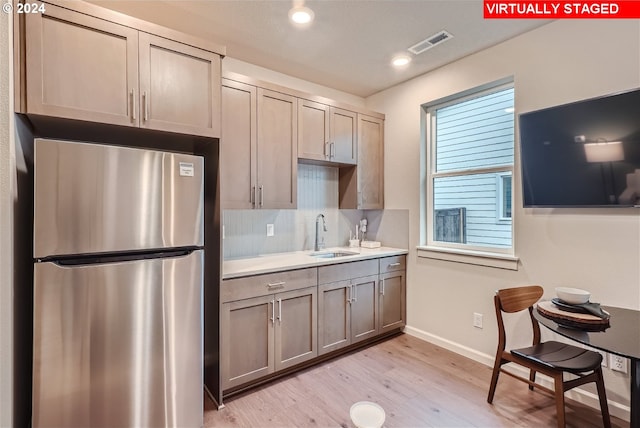 kitchen with backsplash, sink, light wood-type flooring, and stainless steel refrigerator