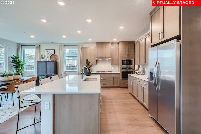 kitchen featuring a kitchen island with sink, a kitchen breakfast bar, light hardwood / wood-style flooring, stainless steel appliances, and sink