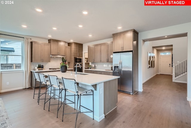 kitchen featuring a breakfast bar, a kitchen island with sink, sink, light hardwood / wood-style floors, and stainless steel appliances