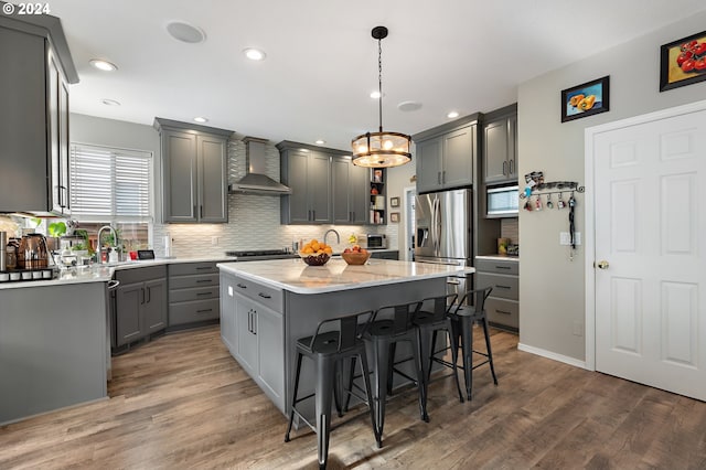 kitchen with stainless steel fridge, gray cabinets, a kitchen island, and wall chimney range hood