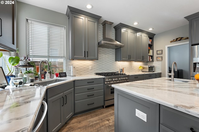 kitchen with gray cabinetry, wall chimney range hood, sink, appliances with stainless steel finishes, and light stone counters