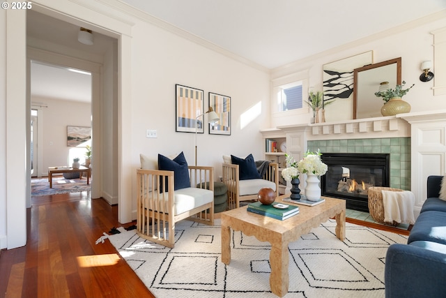 living room featuring hardwood / wood-style floors, crown molding, and a tile fireplace