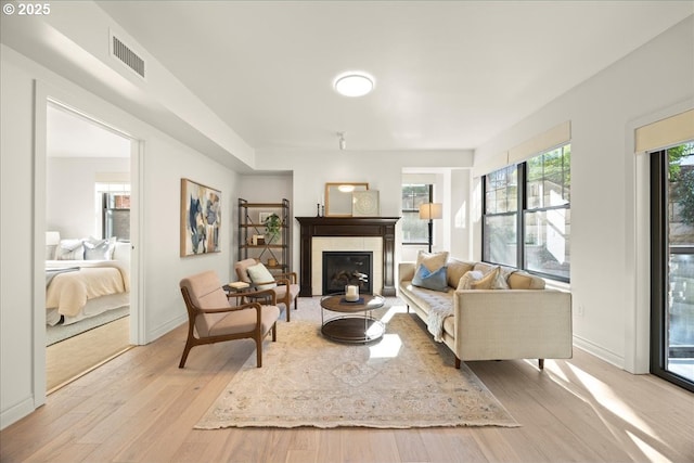 living area featuring light wood-style flooring, a fireplace with flush hearth, visible vents, and baseboards