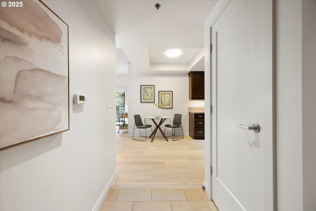 hallway featuring baseboards, a raised ceiling, and light tile patterned flooring