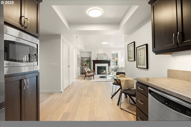 kitchen featuring a fireplace, stainless steel appliances, a raised ceiling, dark brown cabinetry, and light wood-type flooring