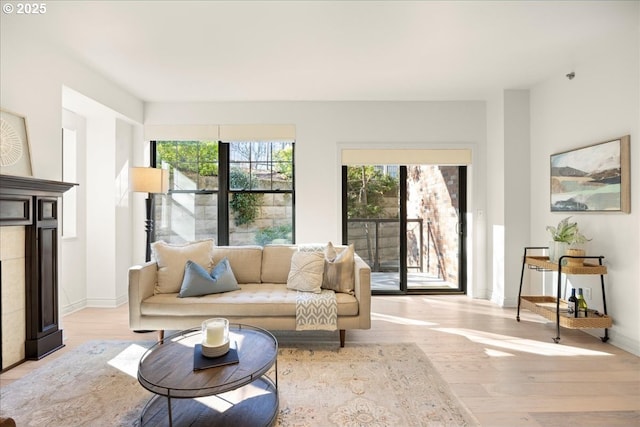 living room with a tiled fireplace, light wood-type flooring, and baseboards