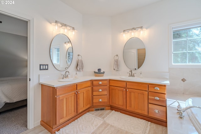 ensuite bathroom with visible vents, double vanity, a sink, and a bath