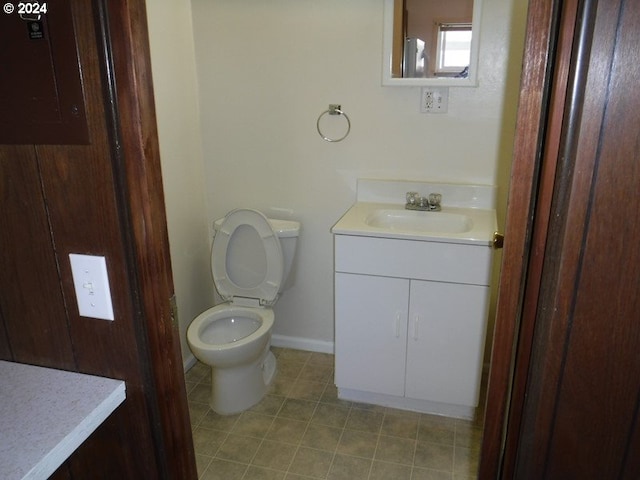 bathroom featuring tile patterned flooring, toilet, vanity, baseboards, and electric panel