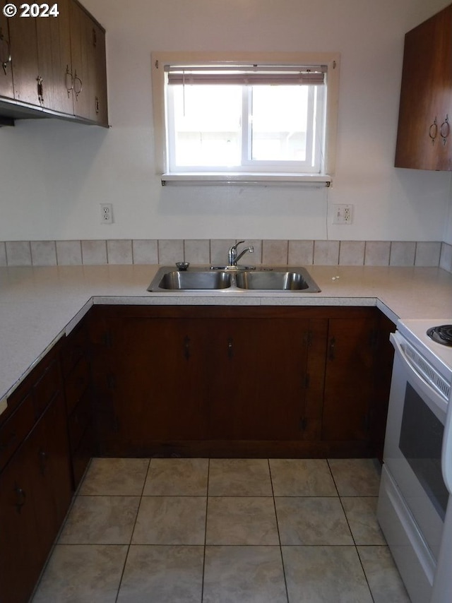 kitchen featuring white electric stove, light countertops, light tile patterned floors, and a sink