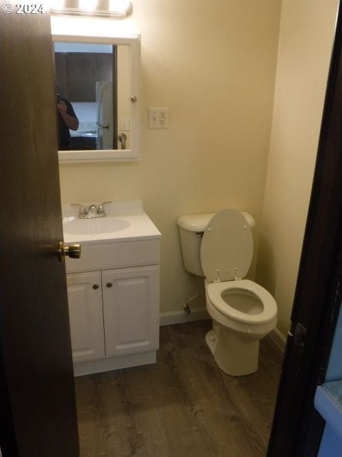 half bathroom with vanity, wood finished floors, toilet, and baseboards