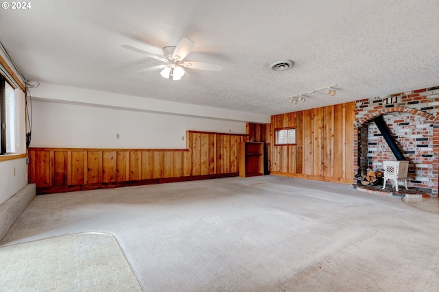 carpeted empty room with wood walls, a wood stove, a textured ceiling, ceiling fan, and track lighting