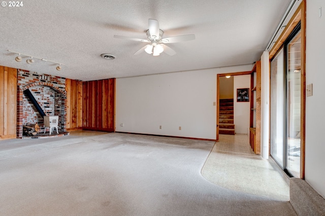 unfurnished living room with wood walls, a wood stove, a textured ceiling, ceiling fan, and light colored carpet